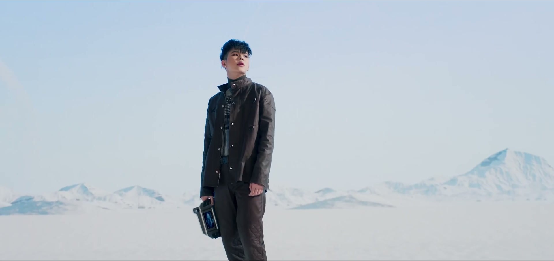 ATLAS stands in a pale desert landscape below snowy peaks in the MAYDAY MAYDAY music video