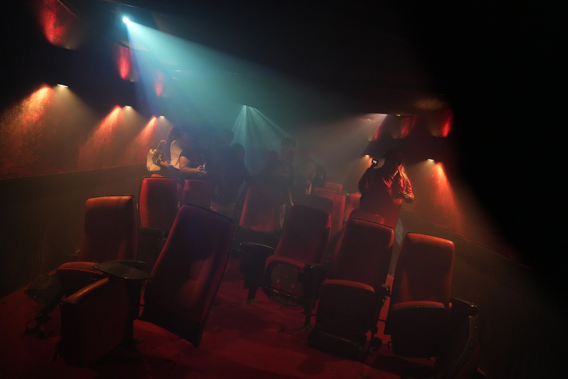 Cinema-style seating inside a TCX 2026 attraction under red and blue light and haze.